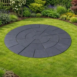 A Black Limestone 3 Meter Circle - 22mm Calibrated patio forms a striking centerpiece in the lawn, bordered by vibrant flower beds and lush greenery for a beautifully landscaped garden.