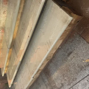 Fossil Mint Sandstone Bullnose Steps 900x350x35mm appear wet, showing water tracks and some dirt. Bordered by a brick wall, the steps lead down to stone paving, with sunlight highlighting their textured surfaces.