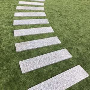 A curved row of Silver Grey Granite G603 Planks (200mm x 900mm) is arranged on green artificial grass, creating a visually striking pattern.