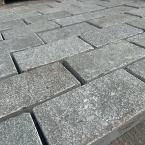 Close-up of Grey Limestone Sawn Edged Setts (200mm x 100mm x 40mm - Sample) arranged in neat rows, creating a flat surface. The setts feature a rough texture and subtly varied grey tones.