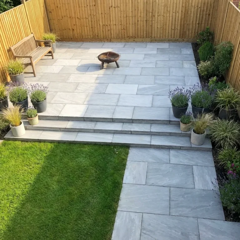 Modern garden with Kandla Grey Indian Sandstone Paving slabs (18mm Calibrated, 600mm x 900mm), a green lawn, potted plants, wooden bench, fire pit, and privacy provided by wooden fencing.