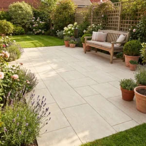 A neatly paved patio with Latte Outdoor Porcelain Paving Tiles (600mm x 900mm x 20mm), surrounded by potted and garden plants, featuring a wooden bench with cushions and a lush, well-maintained lawn in the background.