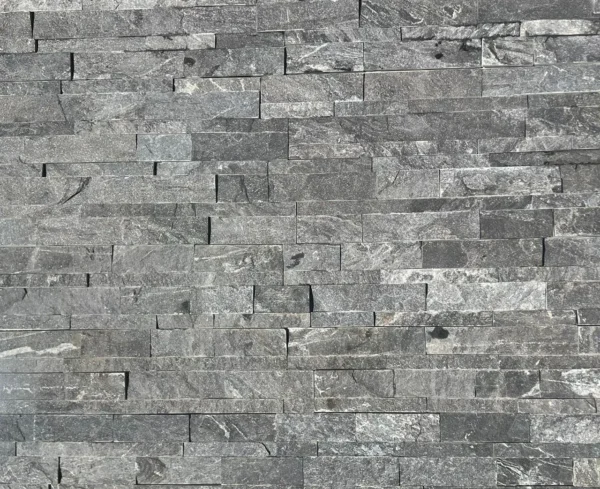 A close-up view of a wall featuring Monsoon Black Stone Cladding, composed of rectangular tiles set in a staggered pattern akin to Indian Sandstone Paving. The tiles display a textured surface, with gentle color variations and natural veining.