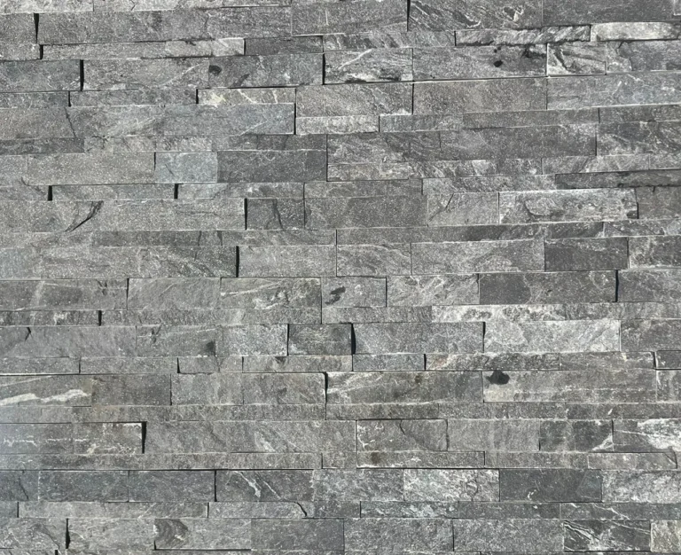 A close-up view of a wall featuring Monsoon Black Stone Cladding, composed of rectangular tiles set in a staggered pattern akin to Indian Sandstone Paving. The tiles display a textured surface, with gentle color variations and natural veining.