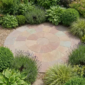 A well-maintained garden features a Raj Green Indian Sandstone 2.4 Meter Circle patio, its concentric stone rings surrounded by lush plants, bushes, and grasses.