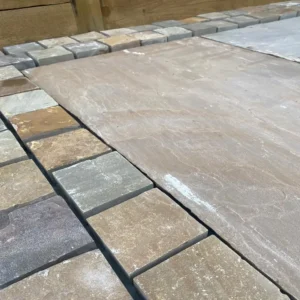 Close-up of neatly arranged Raj Green Sawn Cobble Setts in various shades of brown and gray. The large central cobble has a smooth surface, while the surrounding smaller cobbles display a more textured and varied pattern.