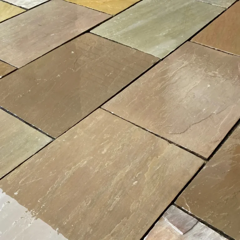 A close-up view of a Camel Buff stone tile floor with rectangular sandstone pieces in shades of brown, gray, and beige. The 22mm calibrated sandstone stones measure 600mm x 900mm and have a slightly glossy finish, creating a varied texture across the surface.