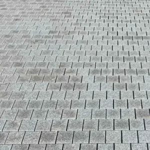 Silver Grey Granite Sawn Edge Cobble Setts (100mm x 100mm x 40mm) are laid in a staggered grid, with their gray rectangular shapes creating a wavy visual effect across the surface.
