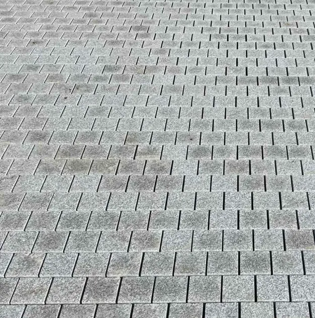 Silver Grey Granite Sawn Edge Cobble Setts (100mm x 100mm x 40mm) are laid in a staggered grid, with their gray rectangular shapes creating a wavy visual effect across the surface.
