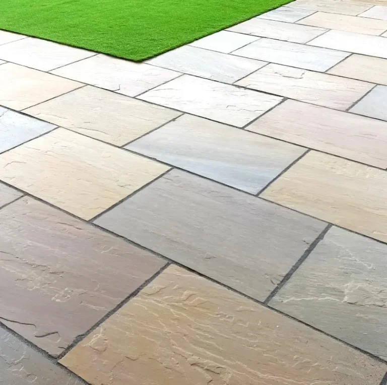 Close-up of a patio featuring Raj Blend Indian Sandstone Paving Slabs (Riven, 18mm Calibrated, 600x900mm) in neutral tones beside vibrant green artificial grass.