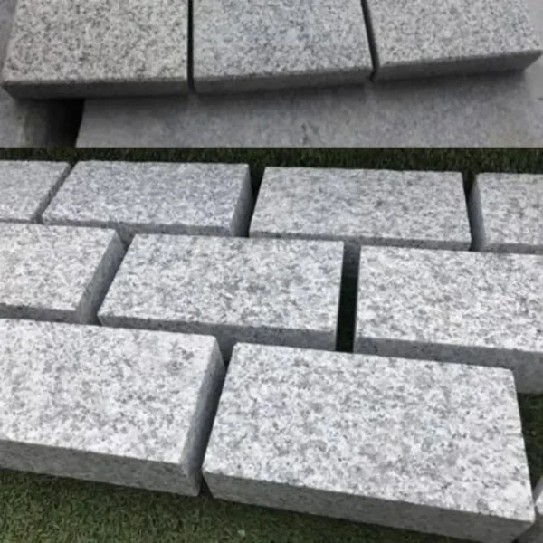 A collection of Silver Grey Granite Setts 200x100 x 40/60 - Sample is exhibited on a surface. Some are arranged in an orderly row on the grass, highlighting their uniform rectangular shapes and rugged, textured surfaces.