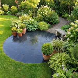 A Black Limestone 3 Meter Circle patio (22mm Calibrated) is surrounded by potted plants, lush shrubs, colorful flowers, a stone bench, and a gravel path winding through the well-maintained garden.
