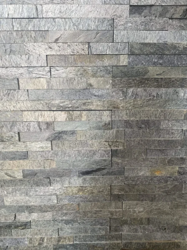A textured wall featuring Silver Shine Stone Cladding made of rectangular grey stone tiles arranged in a staggered pattern, creating a natural and rustic appearance. The slight variation in shade among the stones gives the wall a subtle, multicolored look.