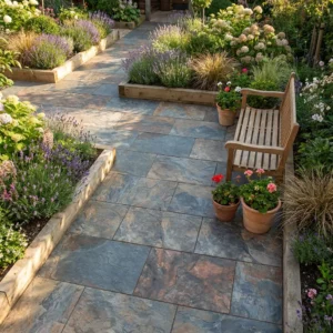 A stone-paved garden path with raised flower beds and greenery, featuring Rustic Slate Porcelain Paving Slabs - 600x900x20mm, and a wooden bench with potted flowers along the walkway.