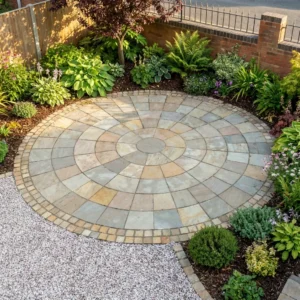 The Yellow Limestone 5 Meter Circle forms a geometric stone patio, bordered by brick edging and a gravel path, surrounded by lush green plants and vibrant flowers in the landscaped garden.